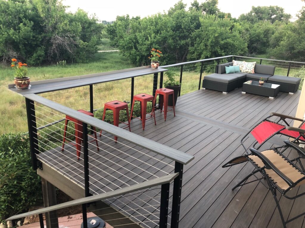 Outdoor deck with black cable railings, bar stools, and sectional seating.