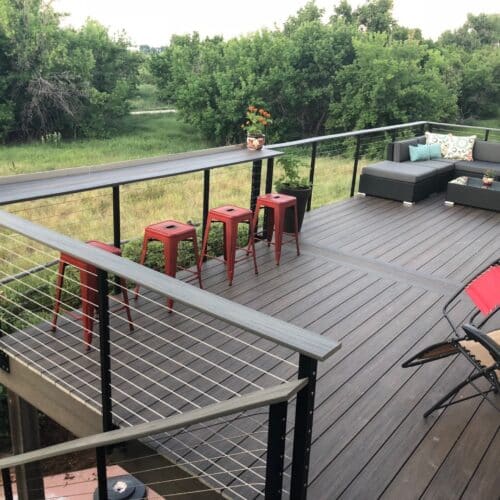 Outdoor deck with black cable railings, bar stools, and sectional seating.