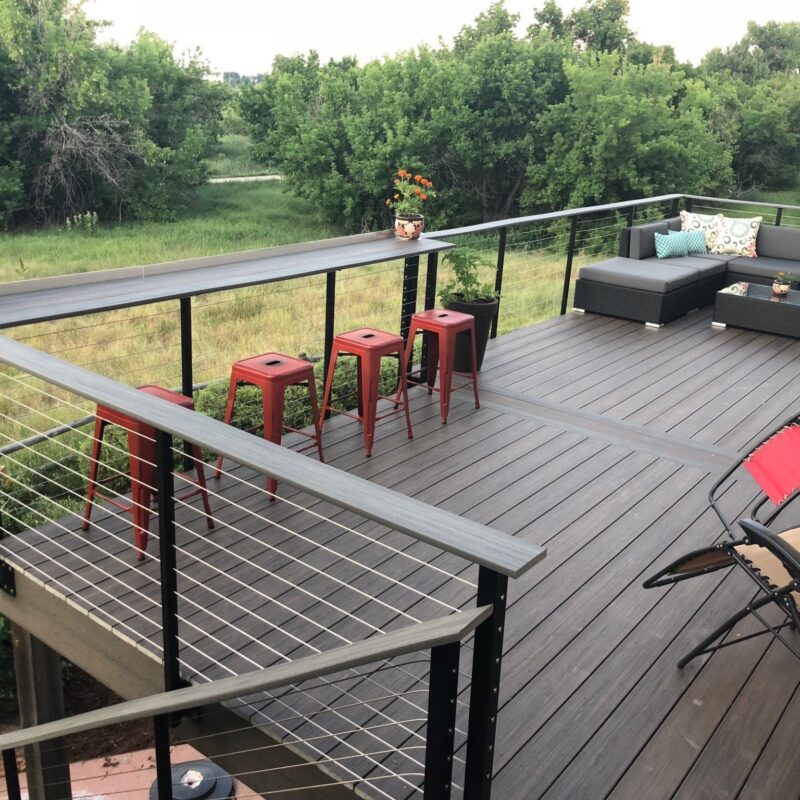 Outdoor deck with black cable railings, bar stools, and sectional seating.