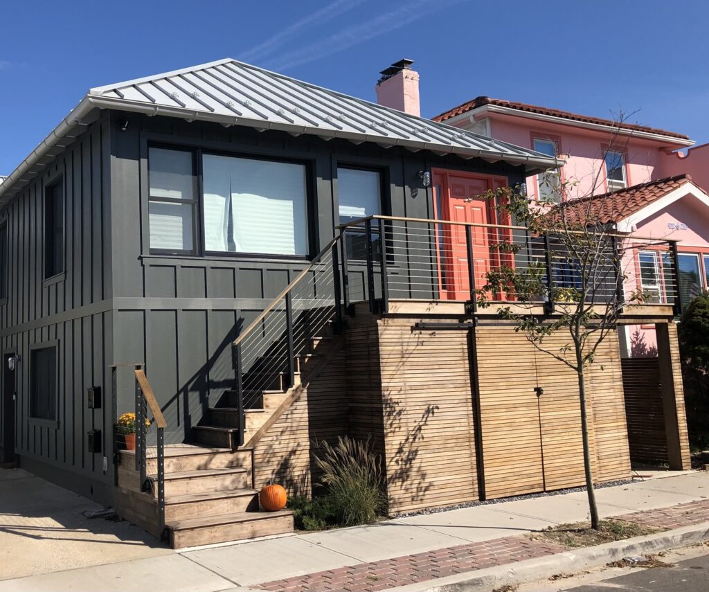 Gray modern house with wooden stairs and balcony framed by black cable railings.