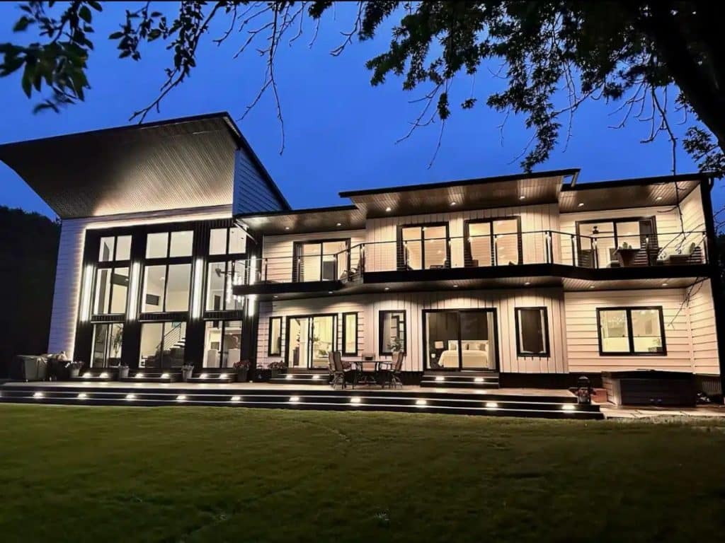 Modern two-story home with balcony cable railings and exterior lighting at dusk.