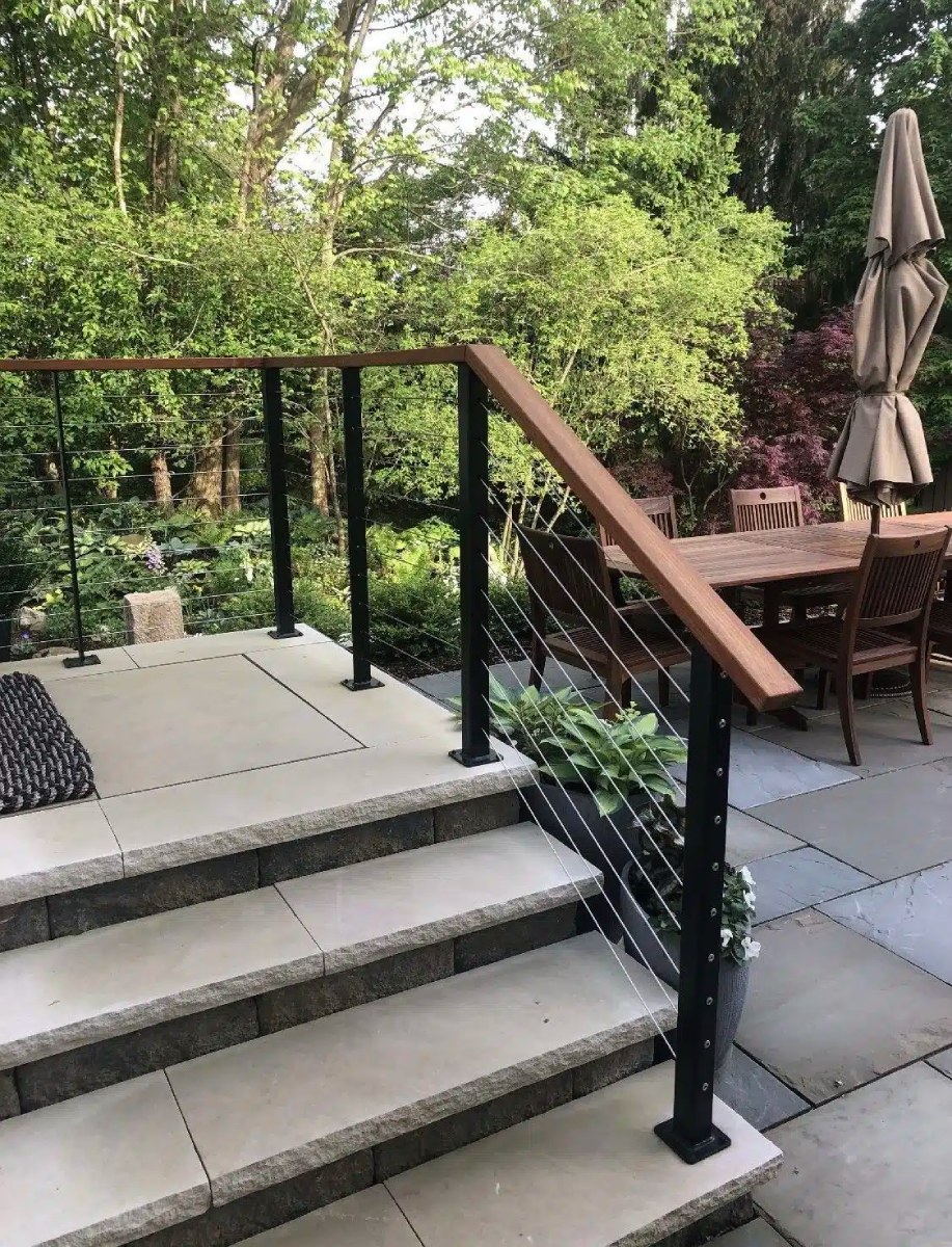 Outdoor patio steps with black cable railings and wooden handrails.